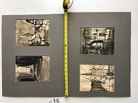 Four small black and white matte paintings mounted on a large grey matte board with a yellow measuring tape showing scale.