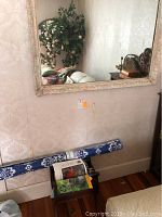 Framed wall mirror hanging on wall with visible slight wear on frame, reflection shows interior setting.