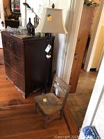 Floor lamp standing next to small wooden chair, placed next to dresser and doorway in room