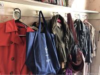 Photo showing 6 jackets in various styles and a navy blue Outriggers book bag hung on hooks.