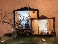 Photo showing both wooden framed mirrors, glass vase with twigs, and floral swag on green surface