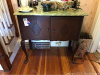 Front view of small wooden cabinet showing two doors, decorative front panels, curved legs, and painted green top with marbled effect.