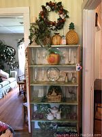 Full view of the shelf with decorative wreath, candle holder, ceramic jars including pineapple and apple, various glassware, cabbage plates, and Peppertime Tea Set arranged on shelves.