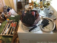 Glass serving platters, purple glass bowl, black trivet, cloth napkins inside the bowl, metal spatula on one platter, white stove in background.