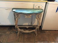 Full view of wood side table with greenish marble-effect painted top against kitchen background.