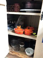 Showcases shelves with orange and purple Pyrex casserole dishes, metal cake pans, and kitchen bowls.