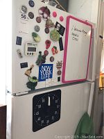Wide shot of refrigerator with various magnets, two magnetic timers, and a whiteboard with pink frame