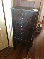 Front view of the dark wood jewelry armoire with seven drawers closed, showing silver knobs and wood grain.