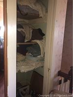 Shelf with folded towels, sheets, blankets, and comforters in neutral colors.