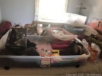 Clear plastic storage bin filled with assorted women's clothing including sweaters, leggings, and slacks.