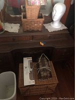 Desk surface with white mannequin head, nested rectangular wicker boxes, and a set of plastic hair curlers on a wicker box.