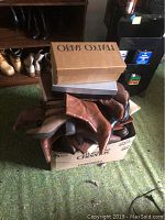 Box with multiple pairs of brown heeled boots piled on top of cardboard boxes.