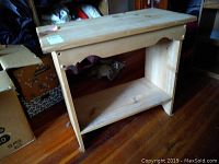 Full view of wooden shelf unit showing two levels and plain wood finish on wooden floor.