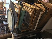Stack of various wooden picture frames, showing different sizes and styles in a basement setting.