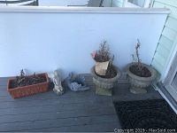 Three outdoor pots including one rectangular terracotta planter and two round concrete urn pots, plus two cement garden ornaments of a rabbit and a bird arranged on a porch floor.