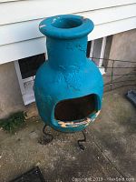 Blue metal clay pot fire pit with metal legs on concrete floor showing paint chipping