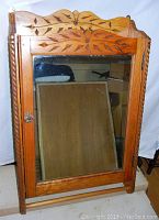 Front view of large wooden medicine cabinet featuring a clear glass mirror on the door and carved decorative details on the top and twisted side columns.