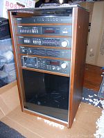 Full view of the Panasonic SE-P9 Hi Fi audio system in wood cabinet with closed glass front showing stacked components and caster wheels at the base.