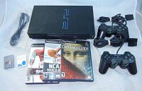 Top view of black Sony PS2 console with blue logo, power cord, 2 memory cards and 3 game cases visible.