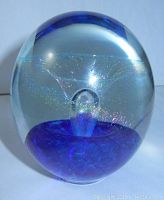 Clear spherical glass paperweight showing deep blue base and internal bubble with iridescent patterns, signed by Eickholt.