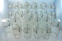 View of 28 mason jars arranged closely, showing varying sizes and consistent clear glass body with wire bail lids