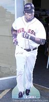 Full view of life size cardboard cutout of David Ortiz, standing approx 6 feet tall in Boston Red Sox uniform outside a building.