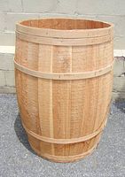Large wooden barrel standing upright on concrete ground with a neutral background, showing full view of barrel's exterior and open top.