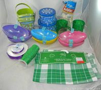 Photo showing assortment of holiday party supplies including egg-shaped containers, green tumblers, metal buckets, ribbons, a table runner, and balloons.