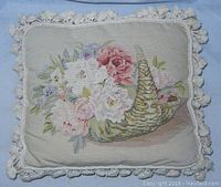 Full front view of the needlepoint pillow showing floral horn basket design with tassels.
