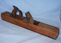 Side angled view showing the full length and profile of the wooden hand plane including handle and blade.
