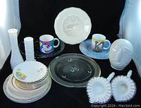 Overview of entire collection showing plates, two white vases, two colorful mugs, two heart-shaped glass dishes, and a clear round plate.