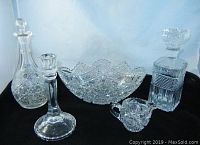 Full view of the lot showing two decanters with stoppers, oval bowl, creamer, and candlestick holder on blue background