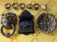 Top view photo showing entire lot of cast iron decorative and functional hardware items including lion door knocker, miniature mailbox, face ashtray, hinges, and knob.