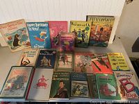 Front view of 18 children's books laid out on the floor in two rows, showing the cover artwork.