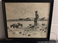 Framed black and white artwork of a man overlooking pack horses in a desert landscape.