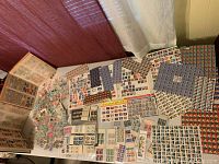 Image showing several opened stamp albums with stamps mounted on pages, loose stamps spread on the table, and full sheets of unused stamps arranged around the albums.