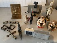 Wide view of the lot showing all items including Hartford Insurance bookend, metal horses, Polaroid camera, ceramic face ashtrays, soldier figurine, metal keychains, arrow-shaped object, whistle and vintage clock.