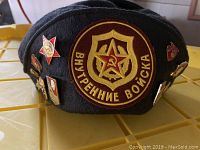 Front and side view of black Russian military hat showing embroidered patch and pins
