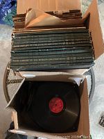 Box with vertically stacked boxed sets labeled 'Basic Library of the World's Greatest Music' with several volumes visible, along with loose records underneath including a 78 rpm record with a red label.