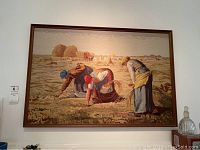 Full view of the framed needlepoint artwork showing three farming women in field with haystacks.