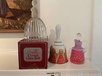 Photo showing three decorative bells: Goebel crystal glass bell on box, Bavaria German angel bell, and pink hobnail decorative bell.
