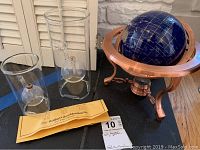 Lot contents including three clear cylindrical glass oil lamps with round reservoirs and one decorative blue glass globe in rose gold stand