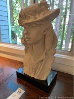 Side view of the bust sculpture showing the hat's floral details and woman's profile.