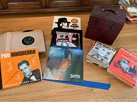 Overview photo showing vinyl records with sleeves, stacked sheet music, and vintage record carrying case.