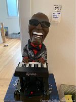 Front view of the Ray Charles motion player figurine seated at keyboard, showing detailed head, sunglasses, suit jacket, and keyboard keys with signature.