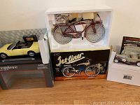 Collection of three models displayed including 1952 Jetliner cast model bike in foam insert, 1932 Cadillac Phaeton die-cast car, and Maisto Thunderbird model car.