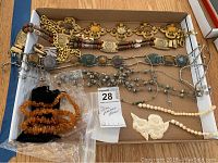 Overview shot showing various belts and necklaces arranged inside cardboard box, including metal belts with semi-precious stones, bead necklaces, and carved pendants.