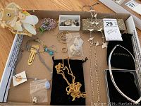 Photo of assorted costume jewelry including necklaces, earrings, pins, and bracelets displayed in a cardboard box.