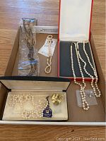 Box containing four necklaces: three white pearl necklaces in original boxes and one black glass beaded necklace in plastic wrap.
