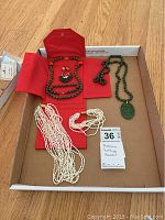 Full view of the jewelry items including green jade bead necklace and bracelet, carved jade pendant necklace, multi-strand rice pearl necklace and bracelet, and black butterfly earrings inside red jewelry case.